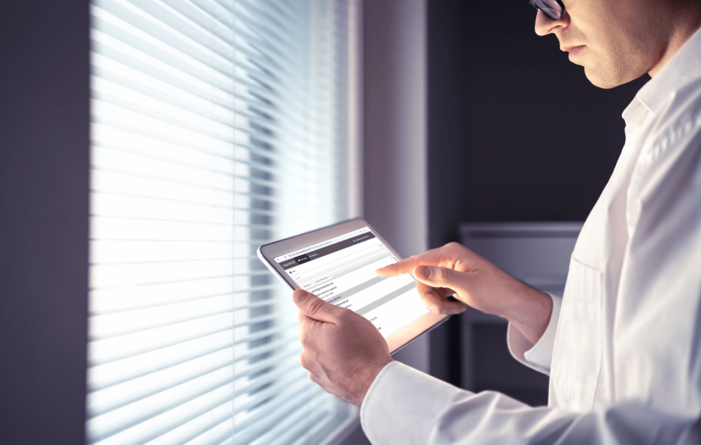 Man uses tablet standing in front of window blinds
