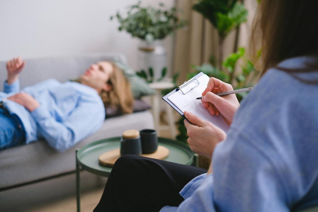 Psychotherapist takes notes while patient talks on couch